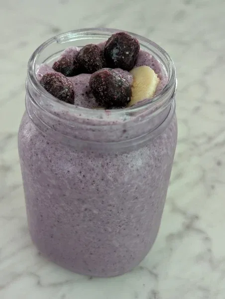 Creamy blueberry banana kefir smoothie in glass cups with fresh blueberries and bananas nearby.